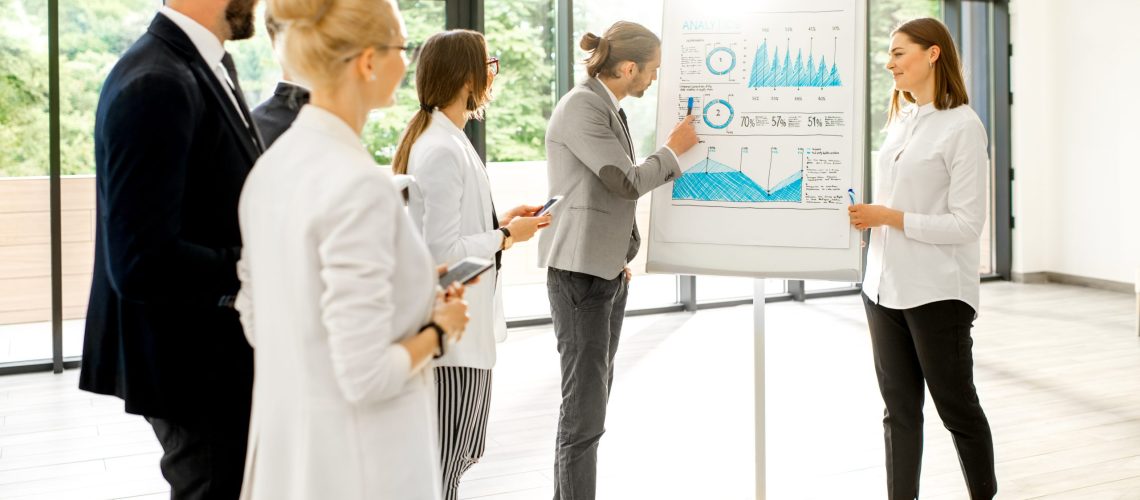 A group of business people standing together during the conference with flip chart at the modern office
